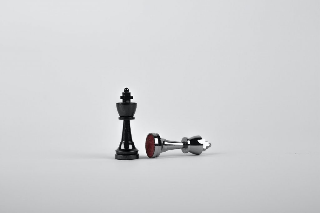 Black king chess piece stands while White king chess piece is fallen
